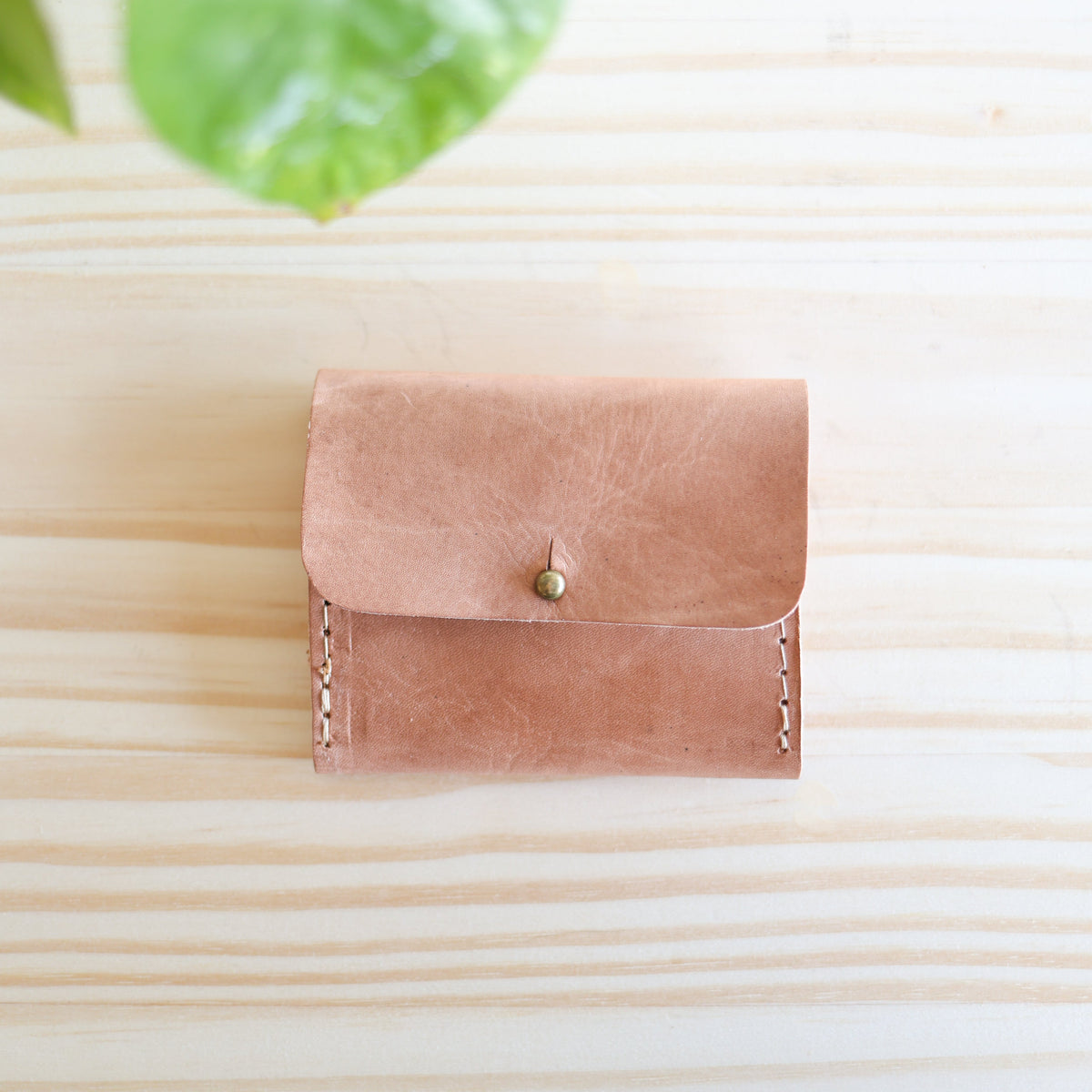 Pink leather wallet on a light wooden surface with green leaves in the corner