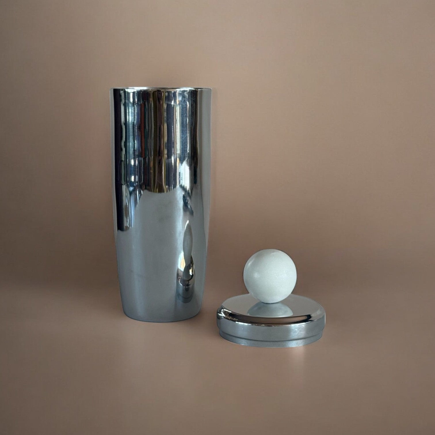 Silver metal cocktail shaker and white marble design on top displayed against a beige background