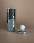 Silver metal cocktail shaker and white marble design on top displayed against a beige background