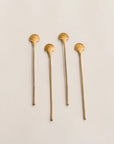 Four gold shell-shaped stir sticks on a beige background