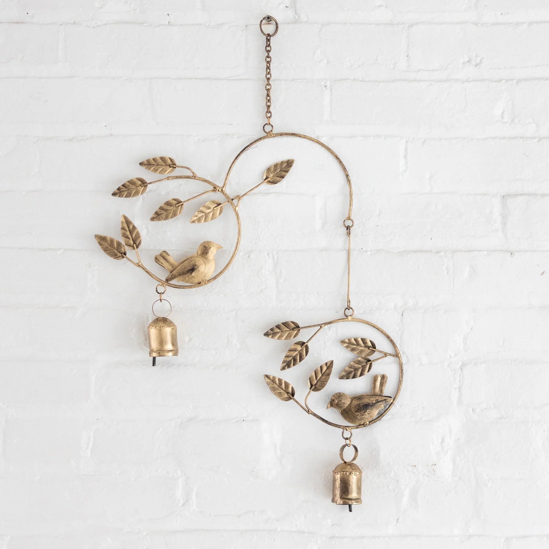 Decorative iron wind chime with birds and leaves on a white brick wall.