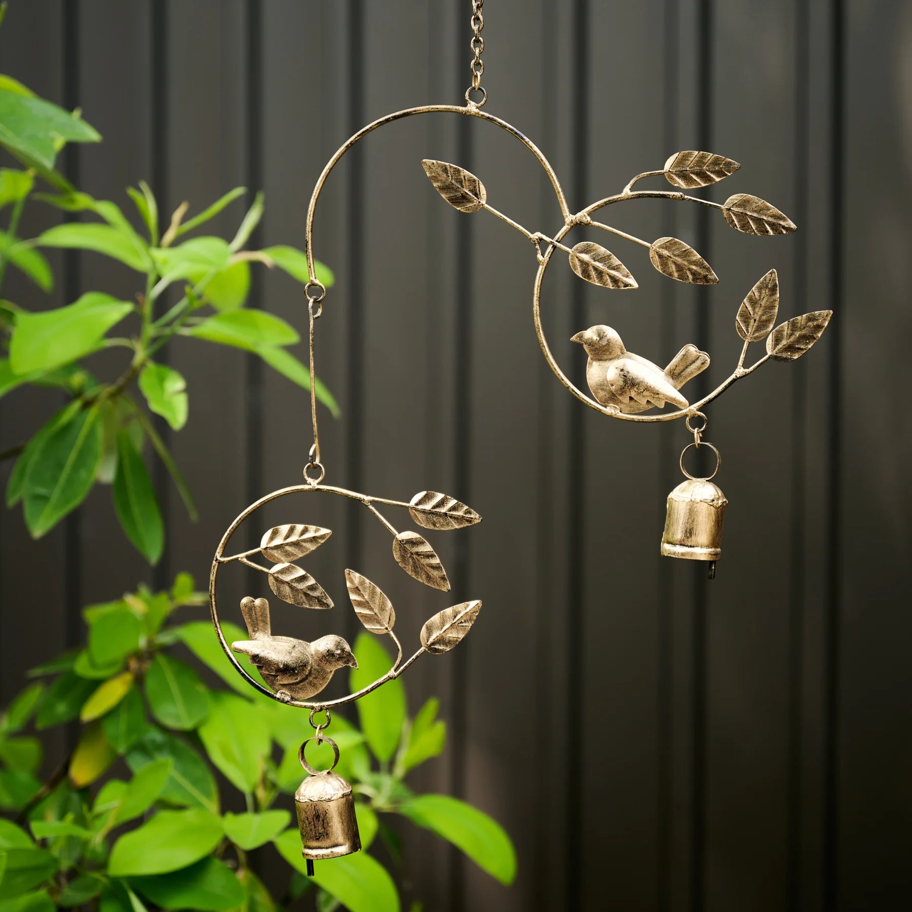 Decorative metal wind chime with birds and leaves against a dark background