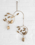 Decorative iron wind chime with birds and leaves on a white brick wall.