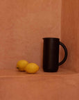 Black pitcher and lemons on a terracotta surface
