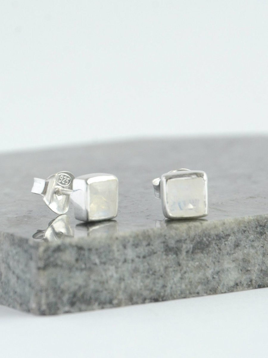 Silver square earrings on a gray stone surface