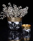 Decorative vase with gold rim and black and white design, accompanied by a small bowl with gold rim on a reflective surface.