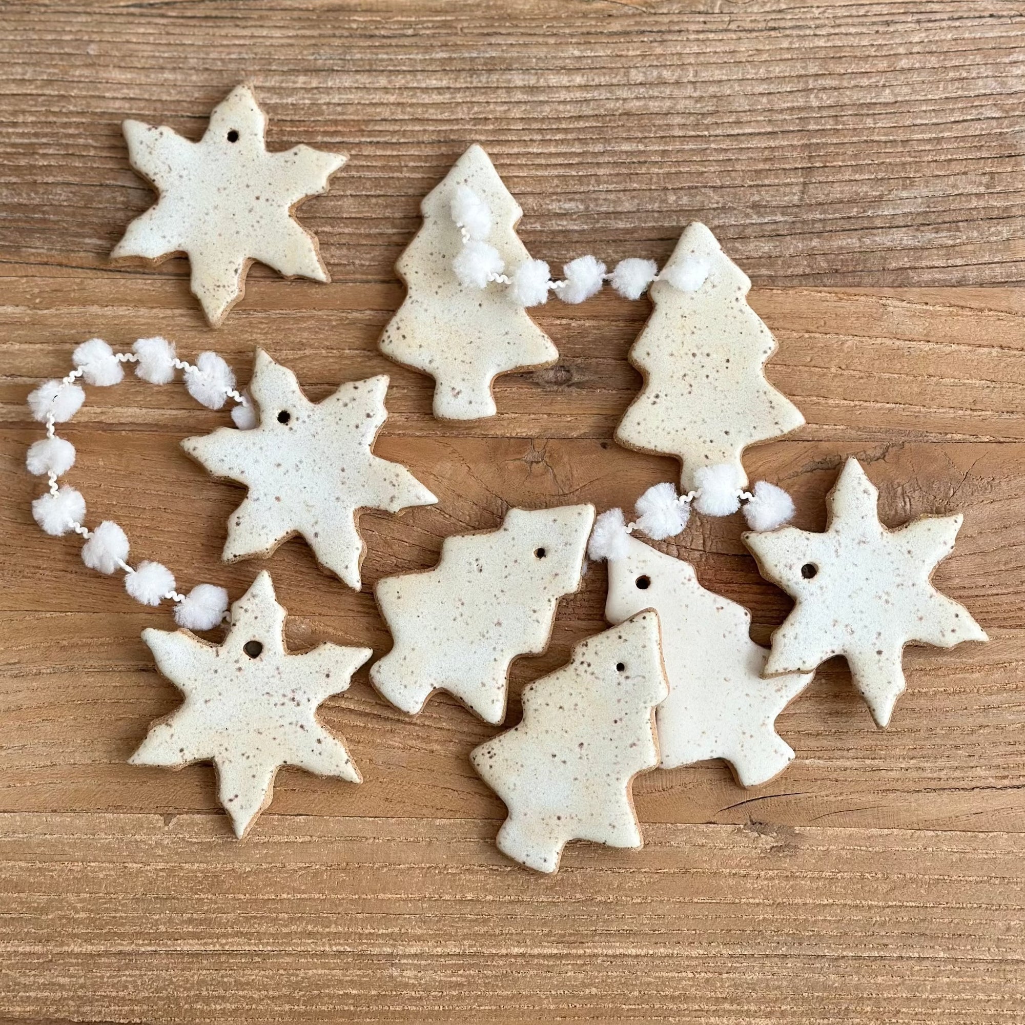 Decorative ceramic ornaments shaped like snowflakes and trees on a wooden surface