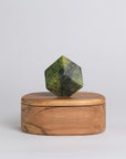 Wooden box with a green geometric stone on top against a light gray background