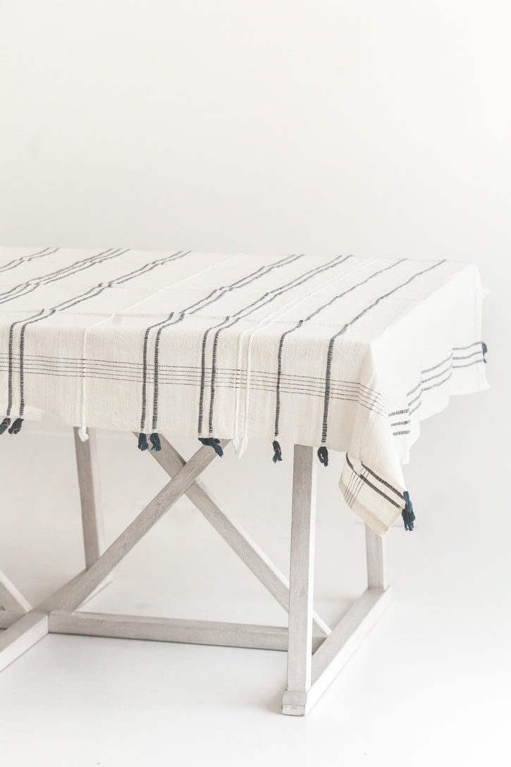 A beige cotton tablecloth with a striped pattern, laid out on a metal frame table against a white background.