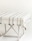 A beige cotton tablecloth with a striped pattern, laid out on a metal frame table against a white background.