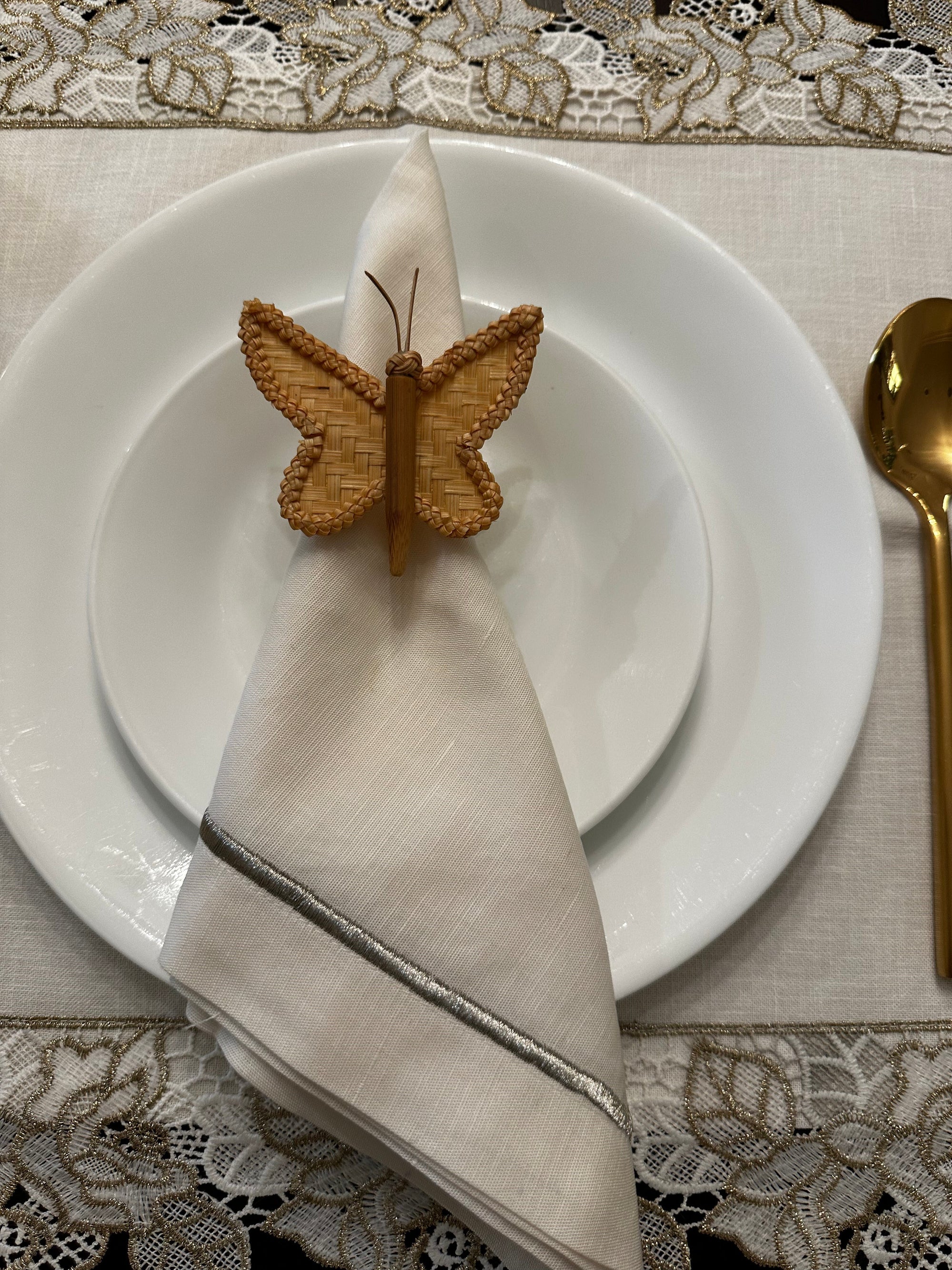 Butterfly-shaped napkin holder on a folded beige napkin over a white plate with a decorative tablecloth.
