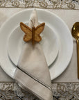 Butterfly-shaped napkin holder on a folded beige napkin over a white plate with a decorative tablecloth.