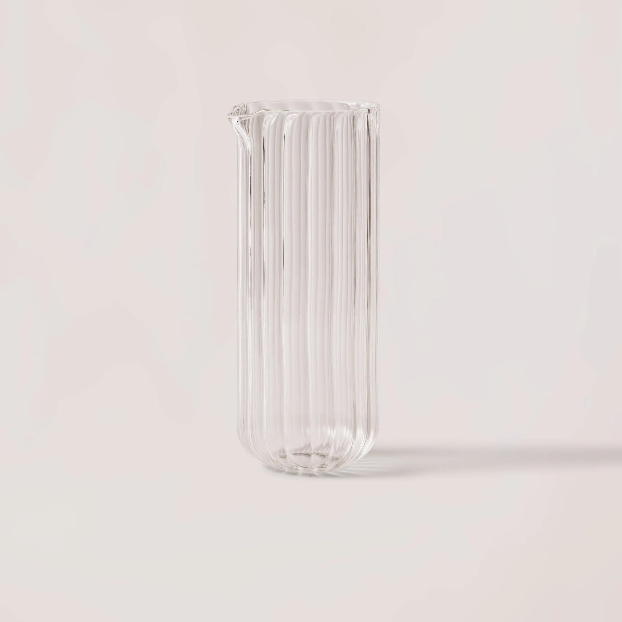Clear glass vase with ribbed design on a light pink background