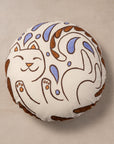 Round embroidered pillow with a cat design on a beige background