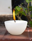 White candle with a single flame on a wooden surface with plants in the background