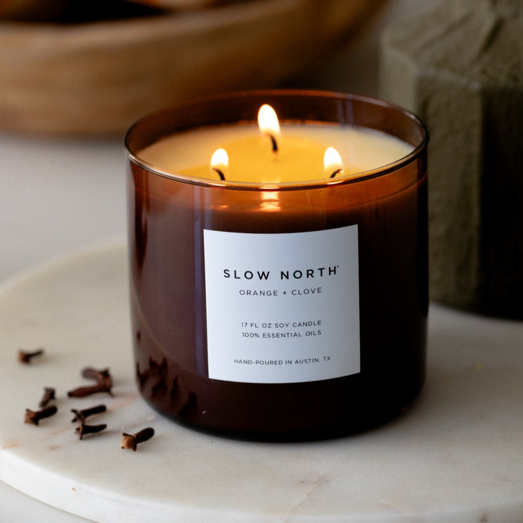 Lit candle in a glass jar with 'Slow North' label on a marble surface
