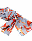 A cotton scarf with a birds design, featuring a mix of orange and red hues on a light blue background.