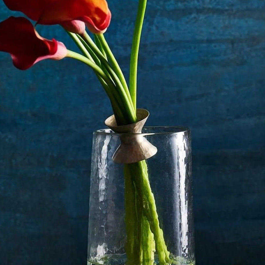 Red flowers in a clear vase attached with a ring on a textured surface with a blue background