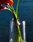 Red flowers in a clear vase attached with a ring on a textured surface with a blue background