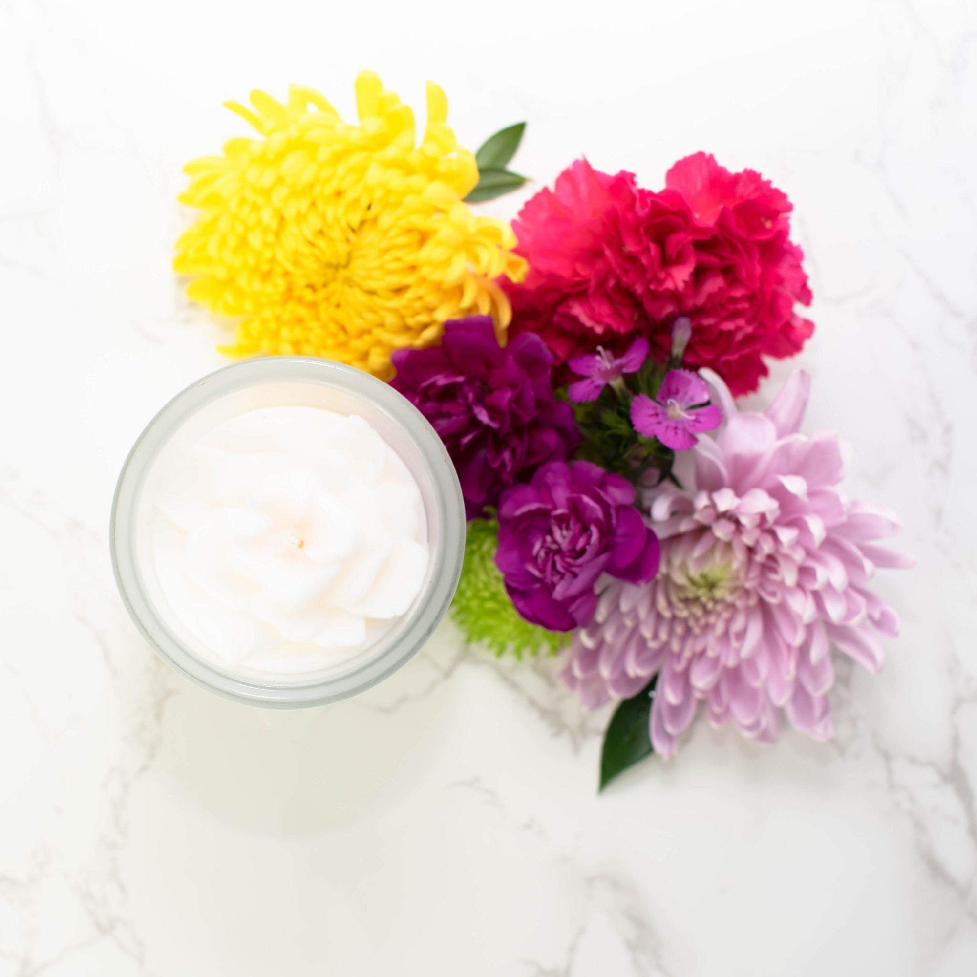 White flower candle on a marble table surrounded by flowers