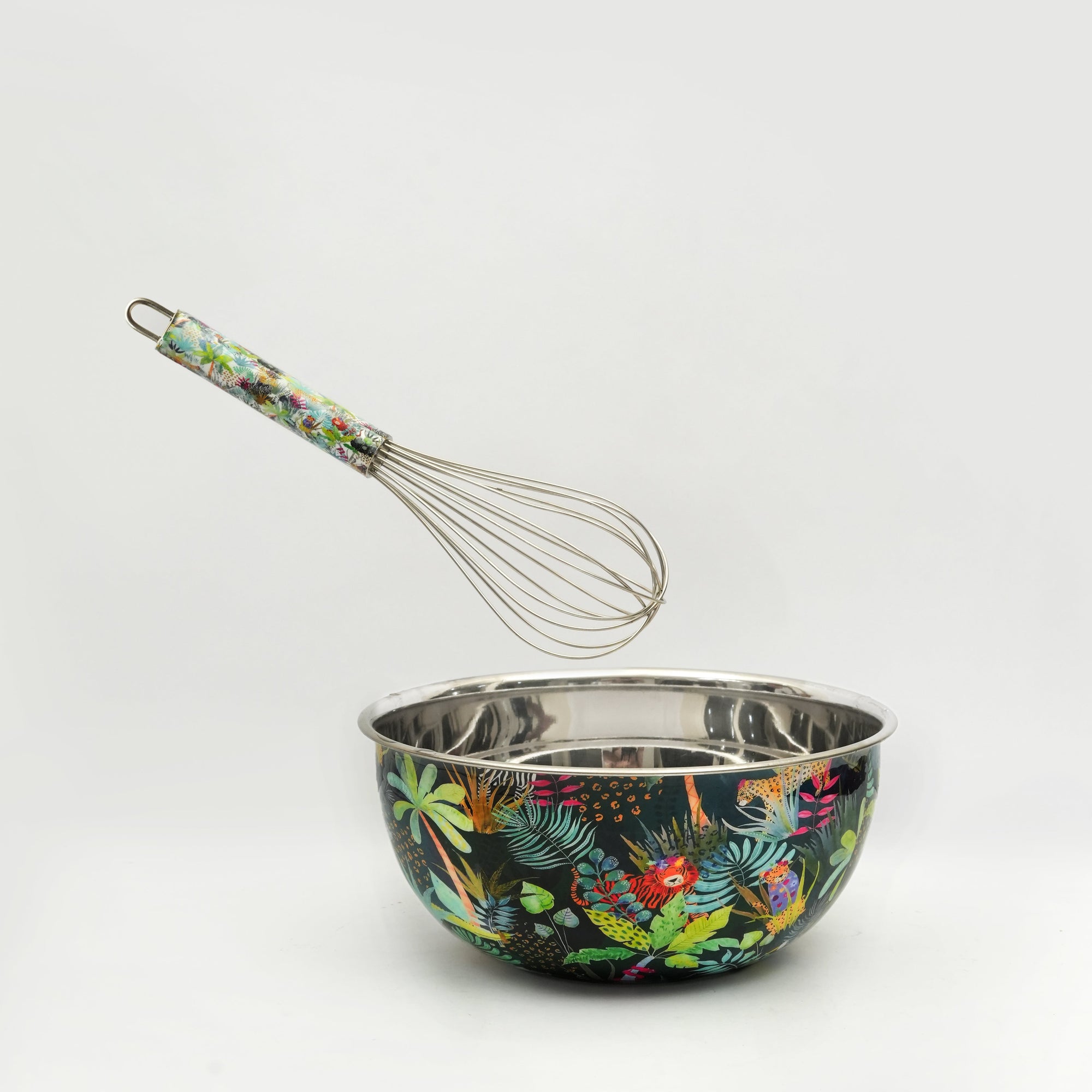 Metal mixing bowl with colorful leaf pattern and matching whisk on a white background