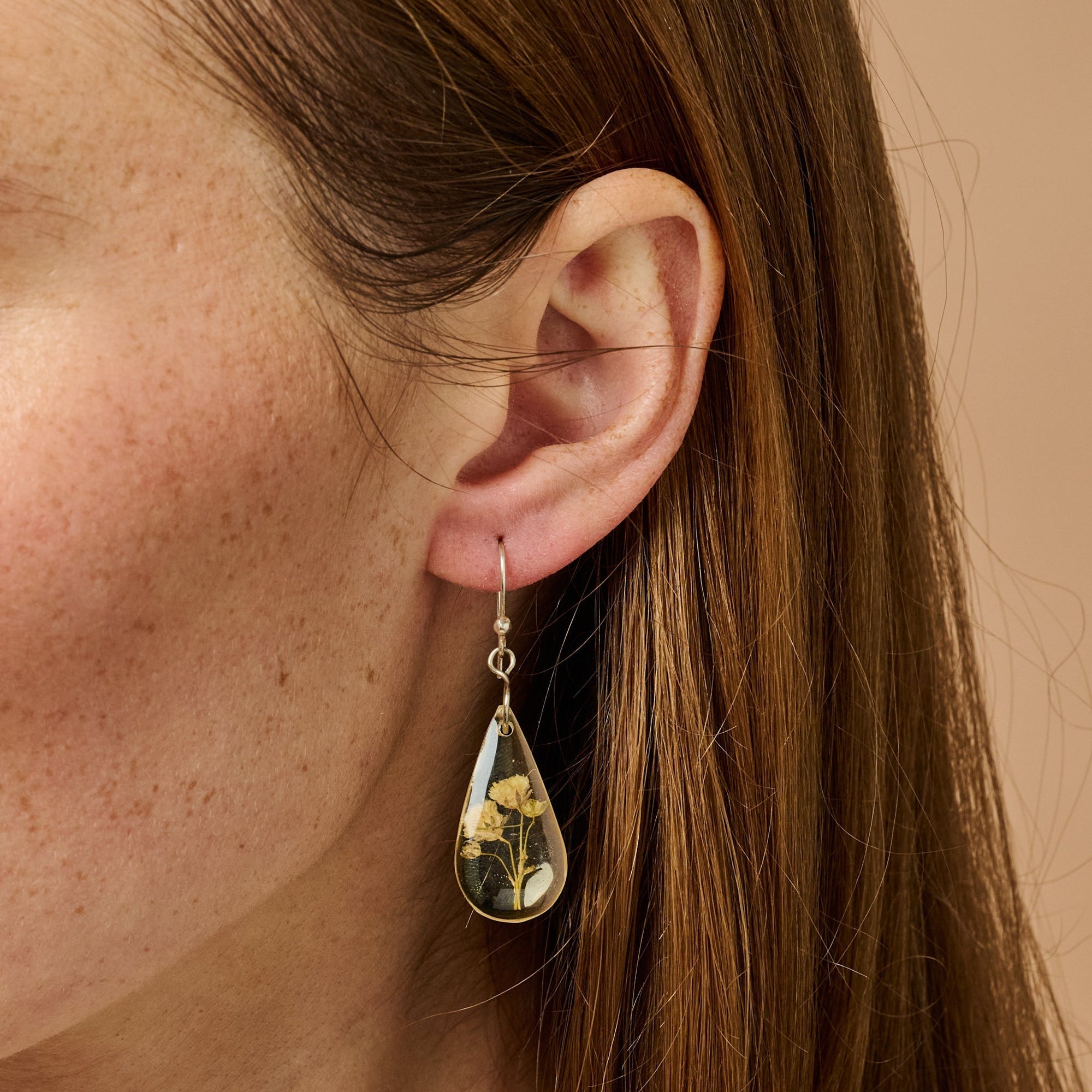 Teardrop-shaped earring with floral design worn by a person with brown hair.
