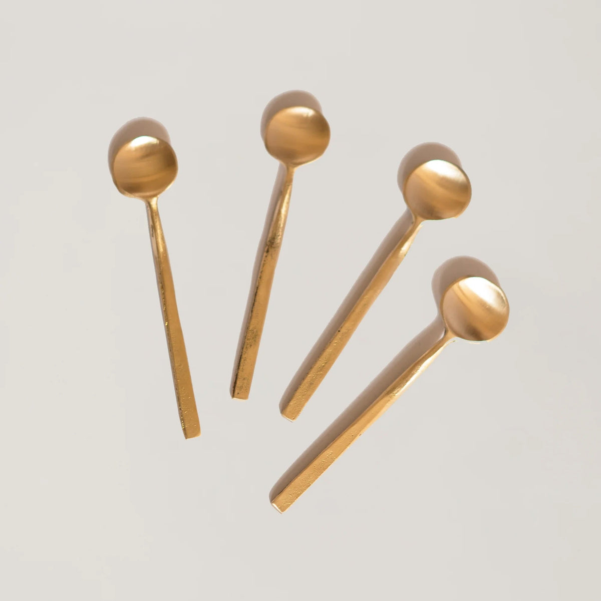 Five gold-colored coffee spoons arranged on a light gray background