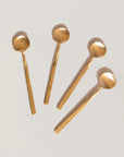 Five gold-colored coffee spoons arranged on a light gray background