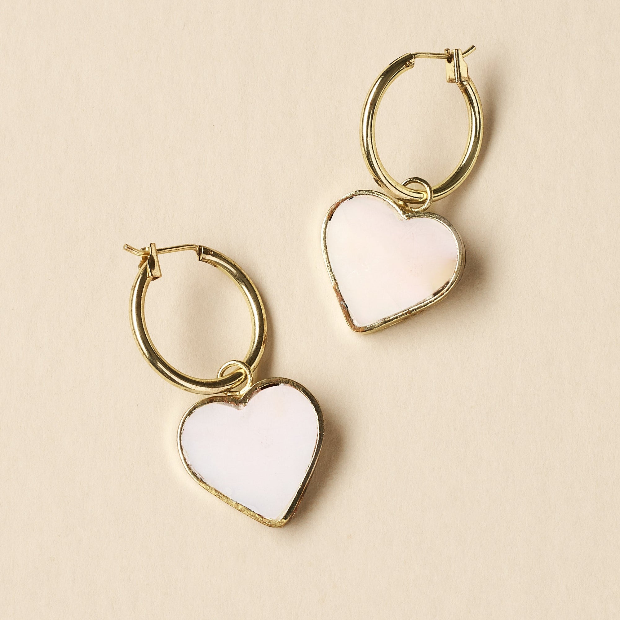 Heart-shaped earrings with gold hoops on a beige background