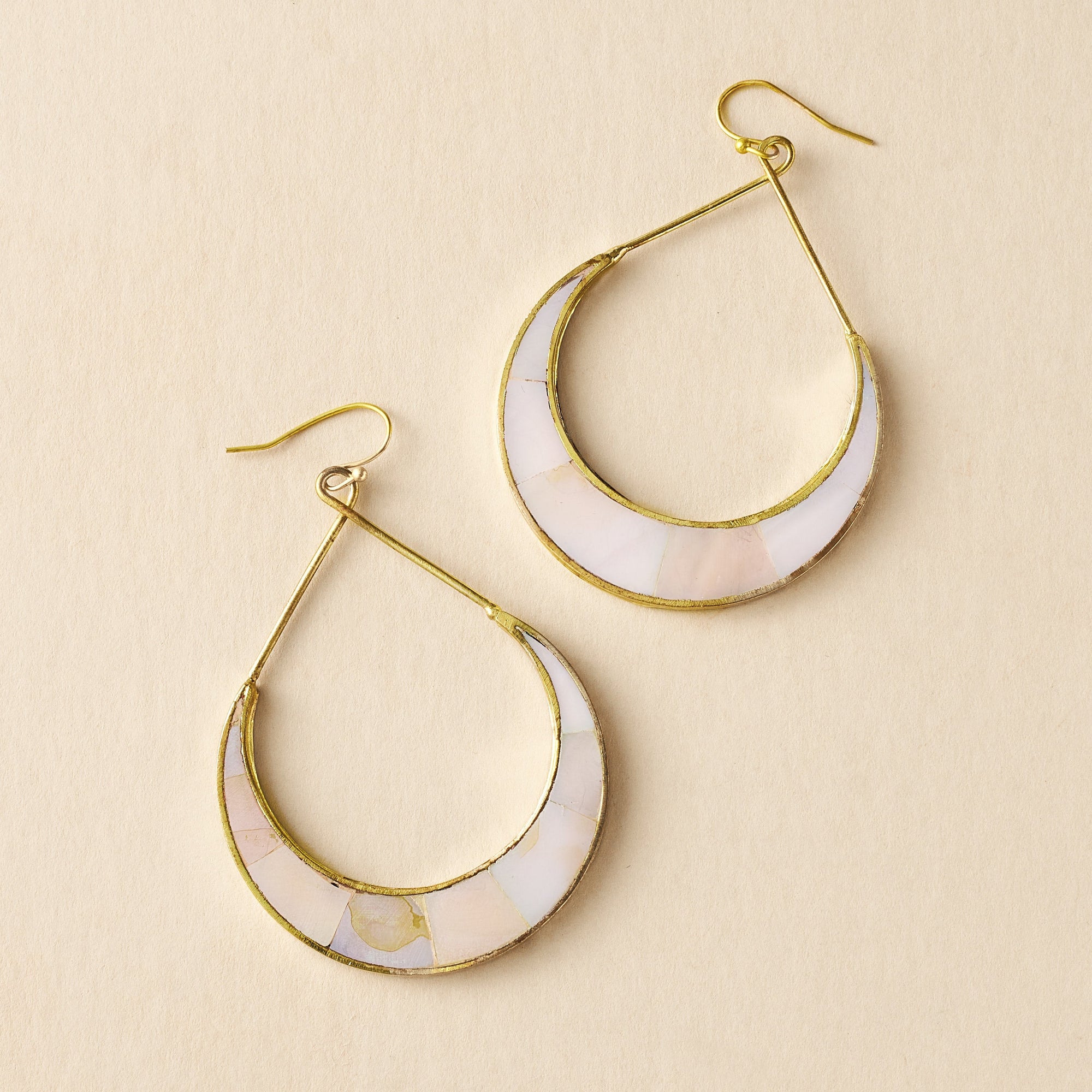 Pair of gold hoop earrings with white stone inlay on a beige background