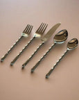 Set of silver cutlery including forks, a knife, and spoons on a pink background