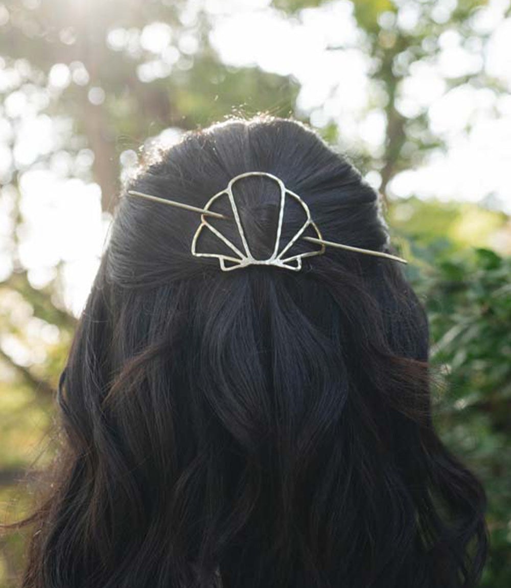 Person with wavy hair wearing a decorative shell design hair pin outdoors