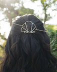 Person with wavy hair wearing a decorative shell design hair pin outdoors