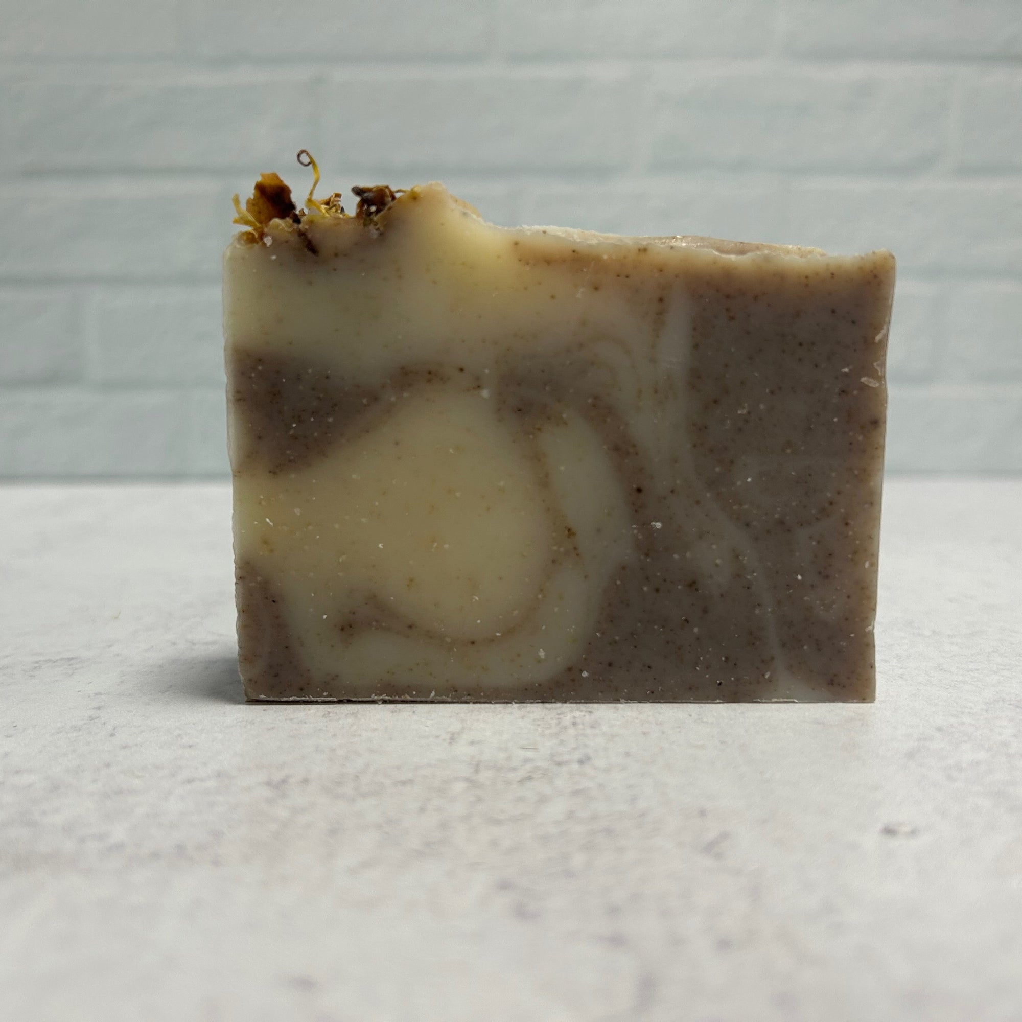 Handmade soap bar with brown and beige swirls on a light gray background