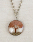 Necklace with a round pendant featuring a tree of life design on a beige background