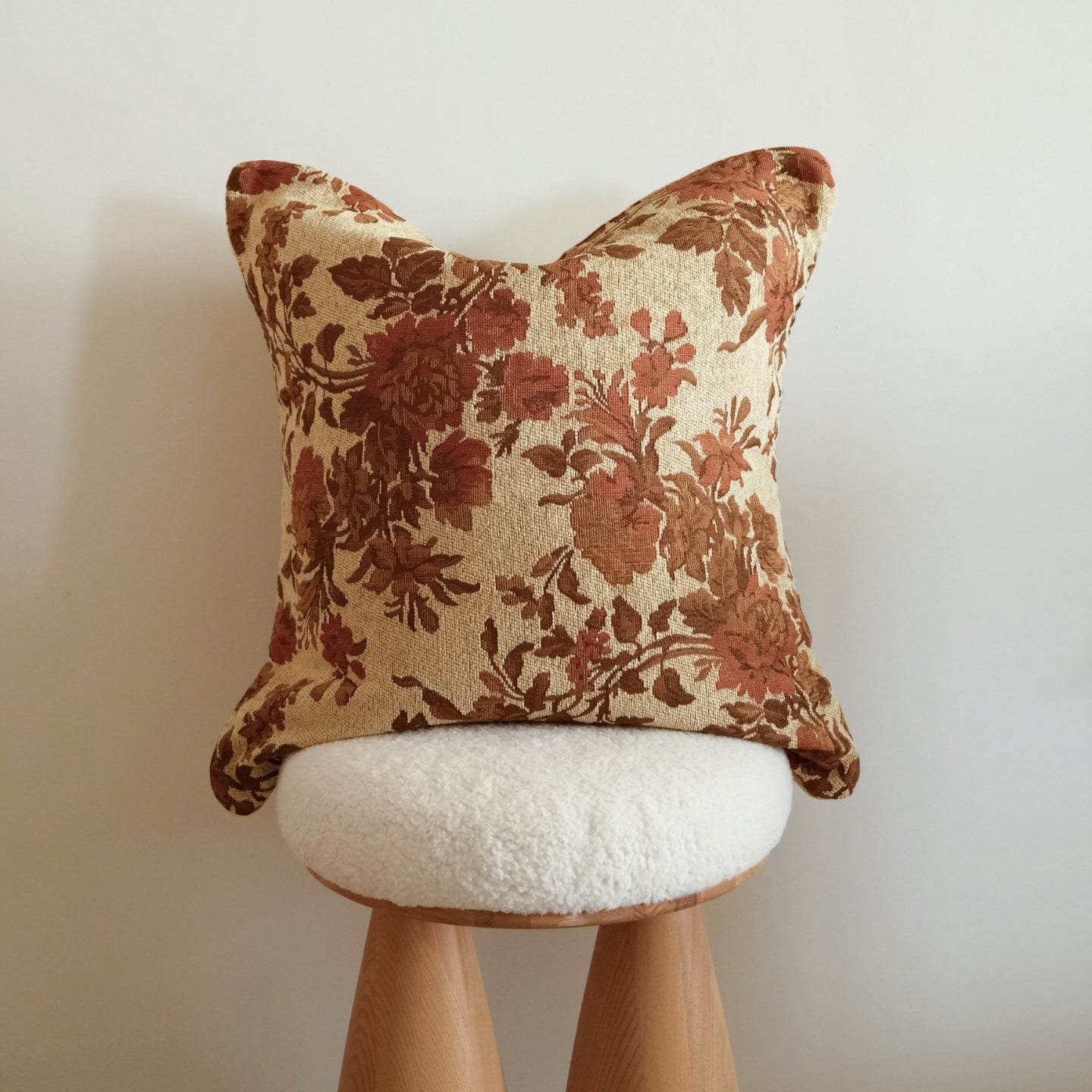 Floral-patterned tapestry pillow on a wooden stool against a plain wall