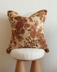 Floral-patterned tapestry pillow on a wooden stool against a plain wall