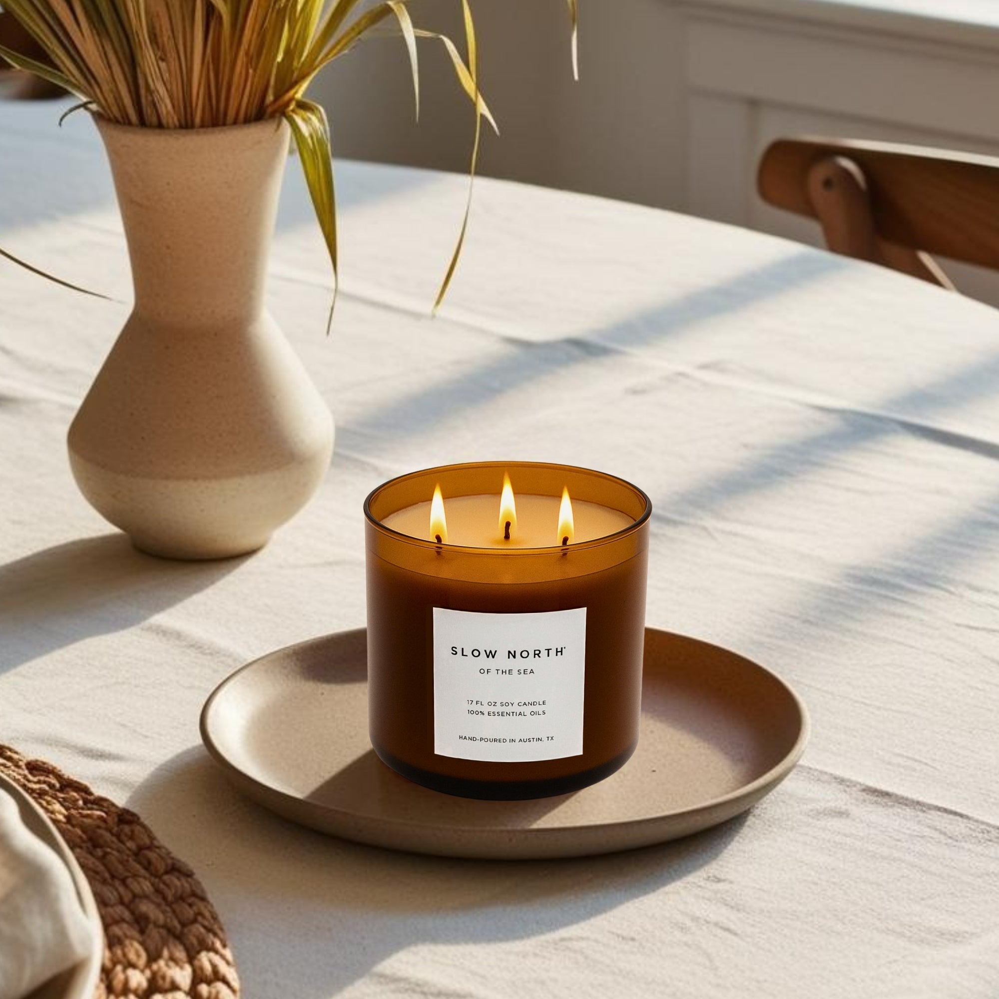 Triple wick candle with 'Slow North' label on a table with a vase and plant in the background
