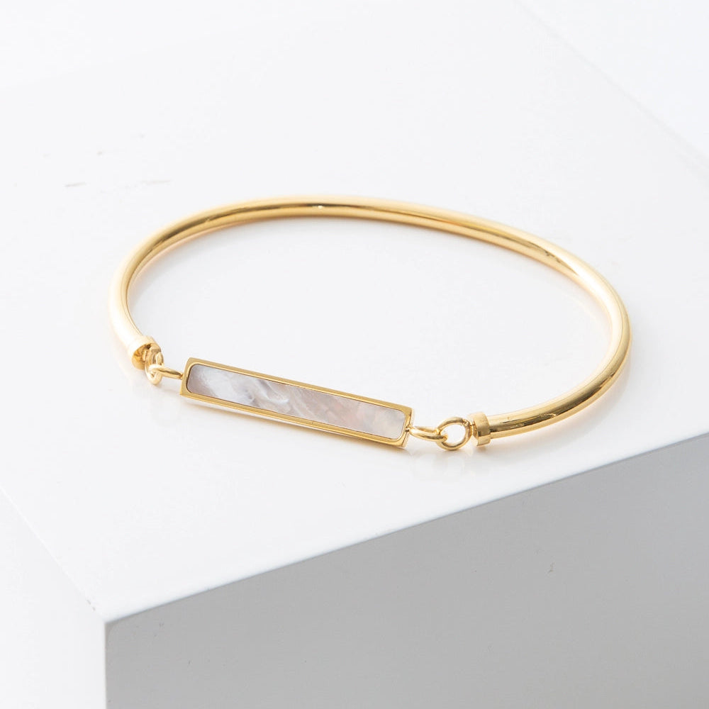 Gold bracelet with a bar design featuring a white pearl on a light gray background
