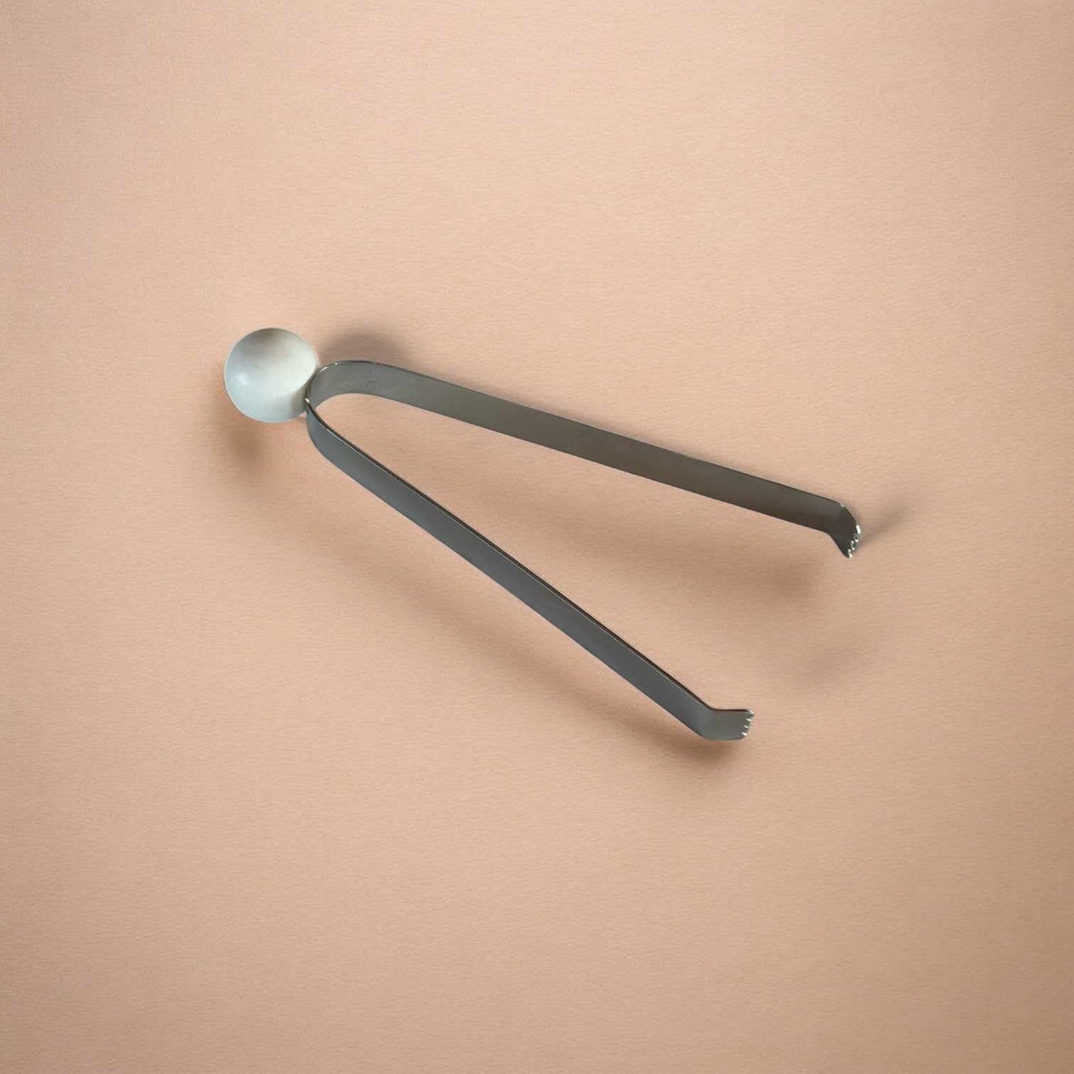 Metal tongs with a round marble head on a beige background