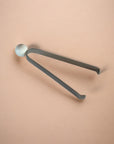 Metal tongs with a round marble head on a beige background