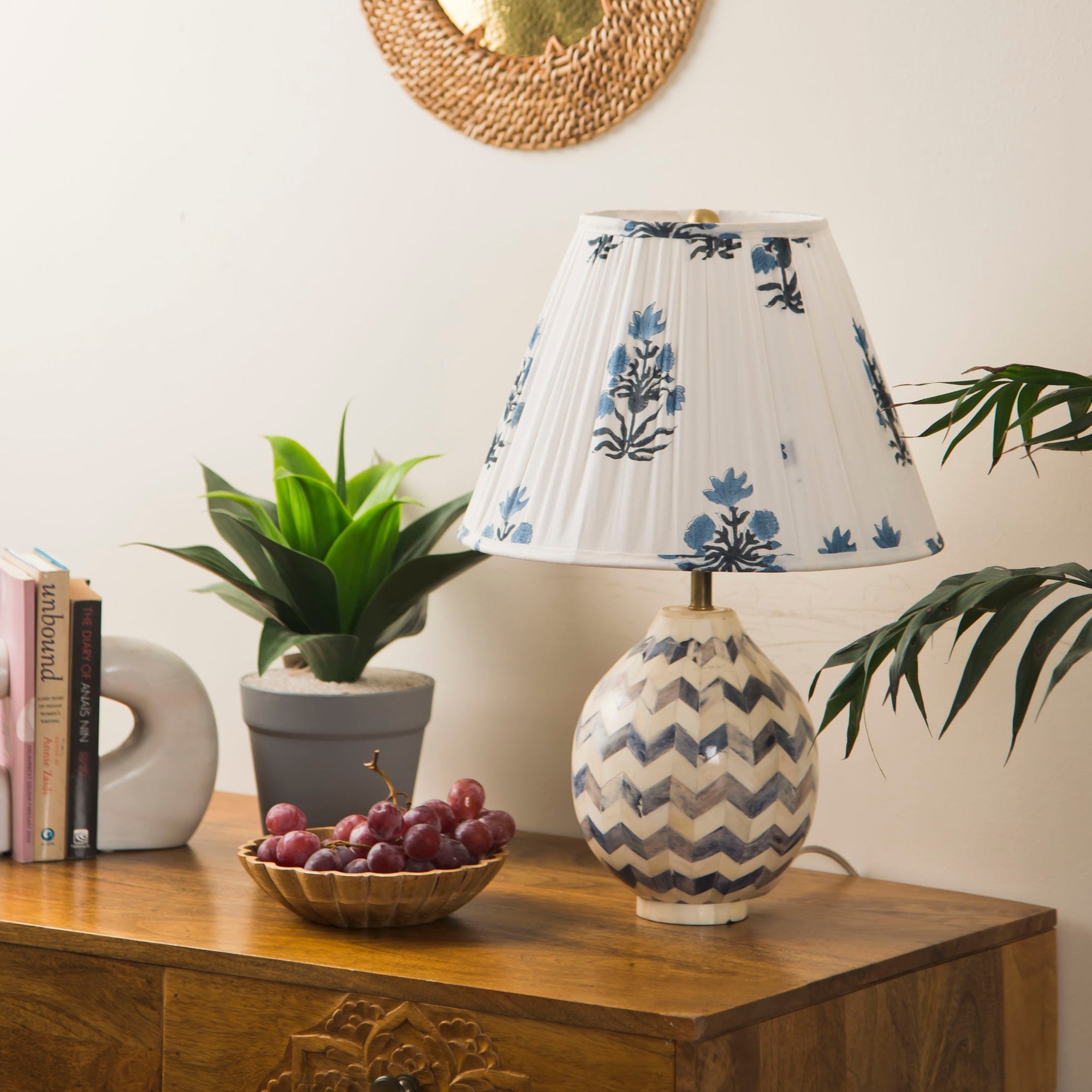 Decorative lampshade  with floral pattern on a wooden table with books and a plant.