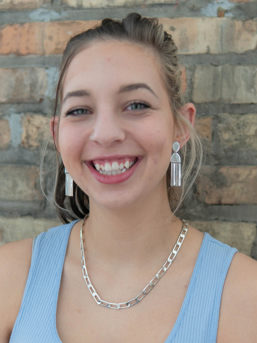 Woman wearing silver earrings and necklace against a brick wall