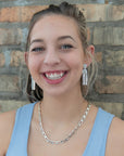 Woman wearing silver earrings and necklace against a brick wall