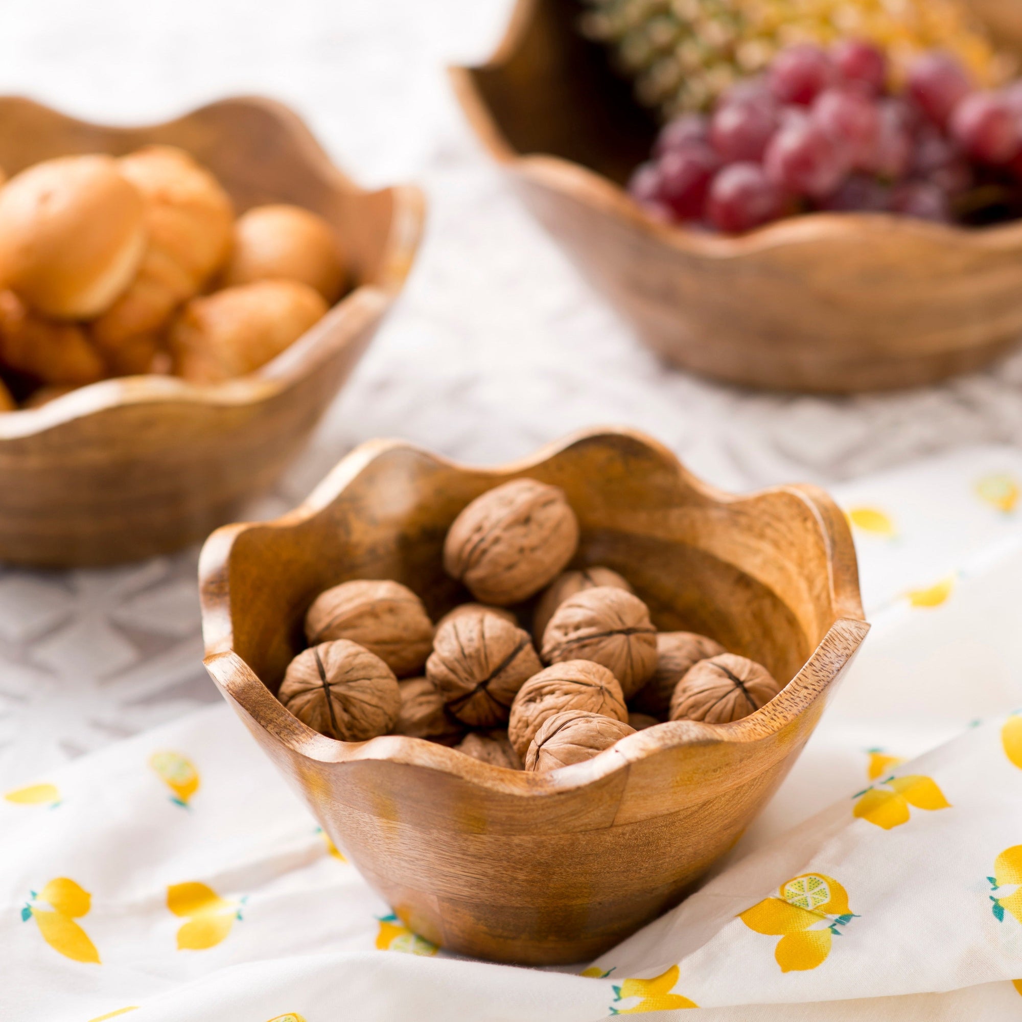 Wooden bowl filled with walnuts on a floral tablecloth with other bowls of fruits in the background