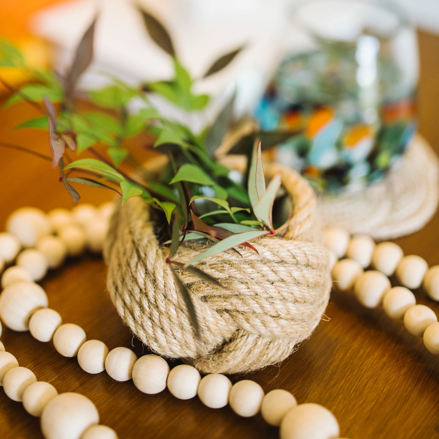 Decorative plant pot wrapped in twine on a wooden surface with beads and a blurred background