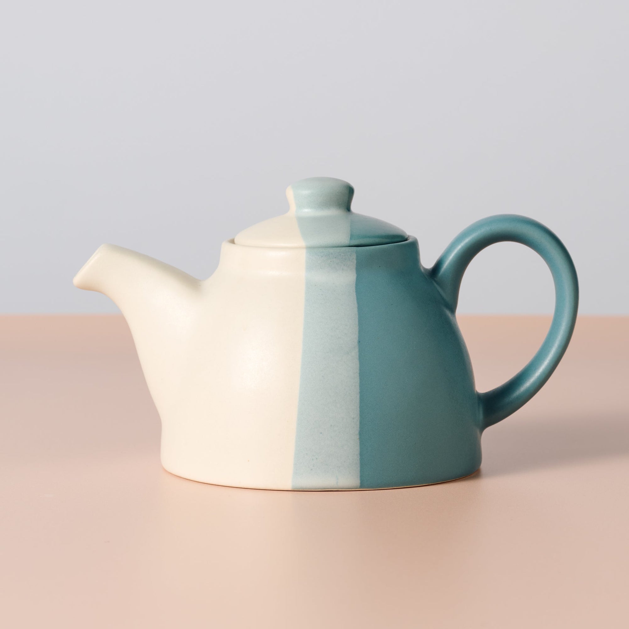Teapot with two-tone design on a beige surface and light gray background