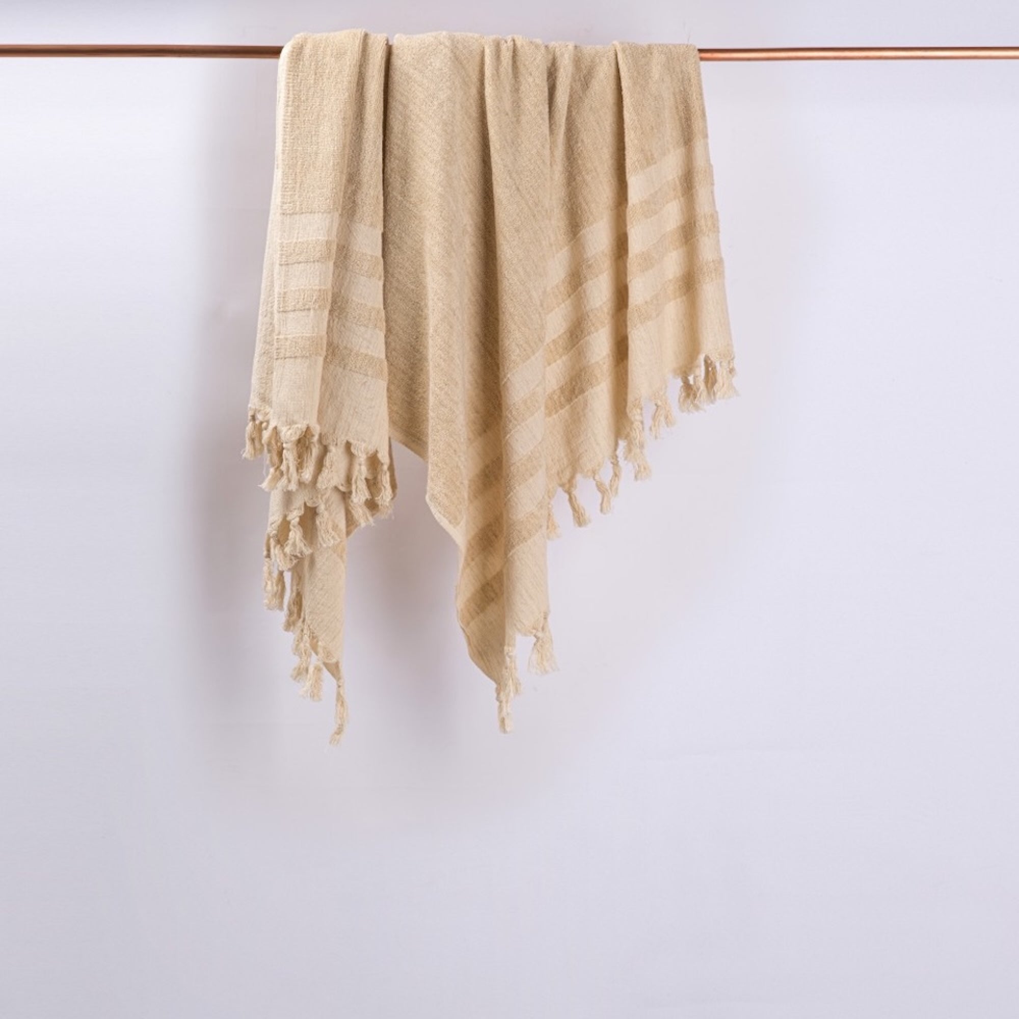 Beige towel with fringes hanging on a wooden rod against a white wall