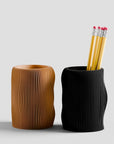 Two textured pen holders, one brown and one black, with pencils inside on a light gray background.