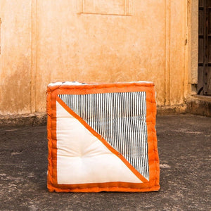 Floor cushion with orange border and striped pattern on a stone floor against a beige wall